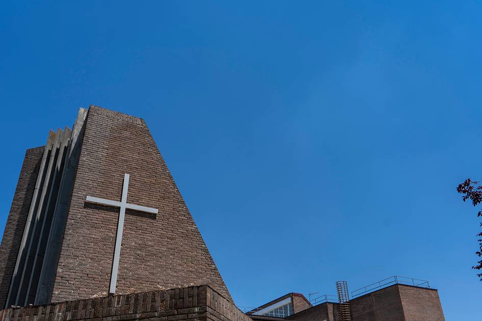 Una iglesia moderna con una cruz visible en su fachada y un cielo azul despejado de fondo.