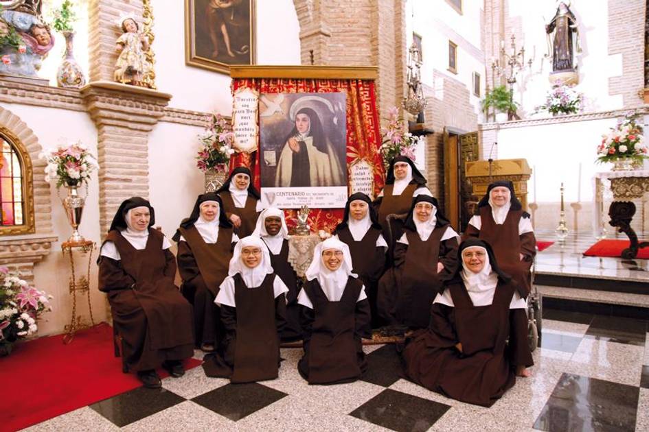 Un grupo de monjas sonrientes posa en una iglesia decorada con flores y retratos.