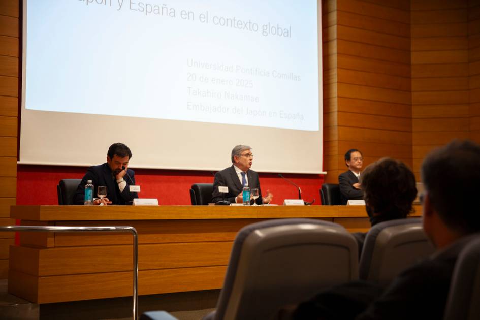 Tres hombres sentados en un panel durante una conferencia en un auditorio.