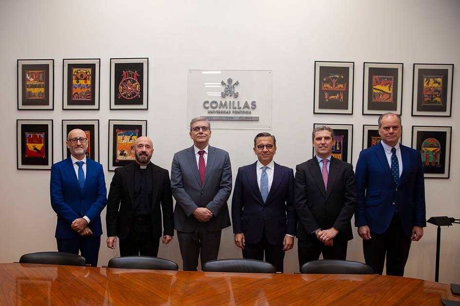 Seis hombres de pie en una sala de reuniones con cuadros coloridos en la pared y un logotipo de Comillas detrás de ellos.