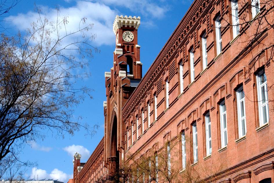 A historic brick building with a distinctive clock tower under a clear blue sky.