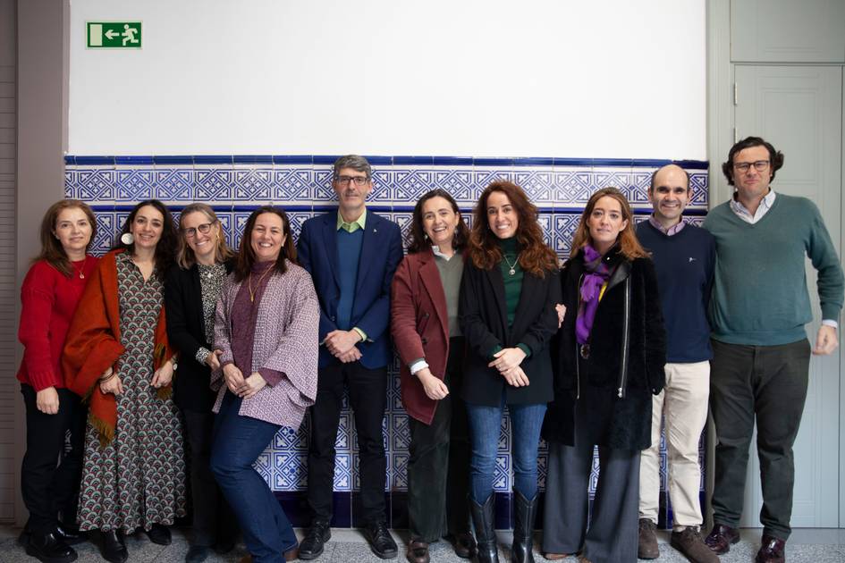 Un grupo de nueve personas sonriendo para la cámara en un pasillo con azulejos decorativos.