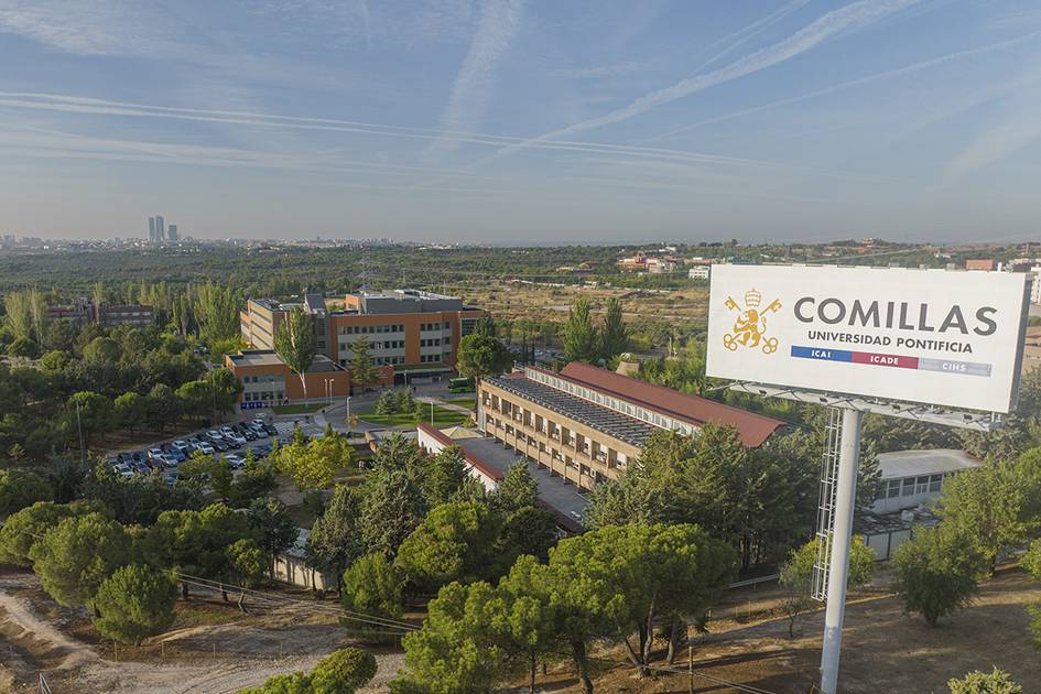 Aerial view of the Comillas Pontifical University campus with a large sign, surrounded by greenery.