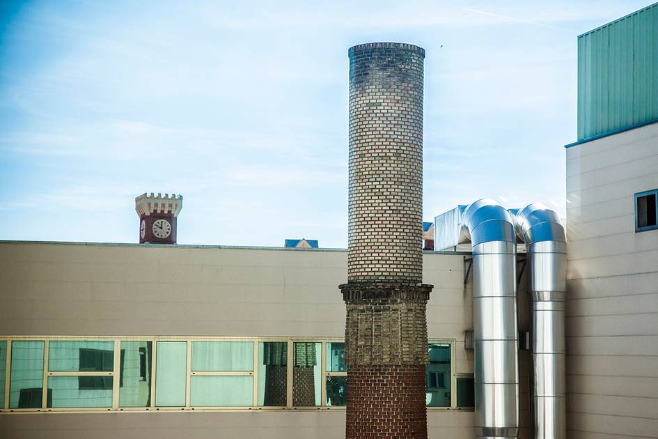 La imagen muestra una chimenea de ladrillo en un edificio moderno con tubos metálicos al lado.
