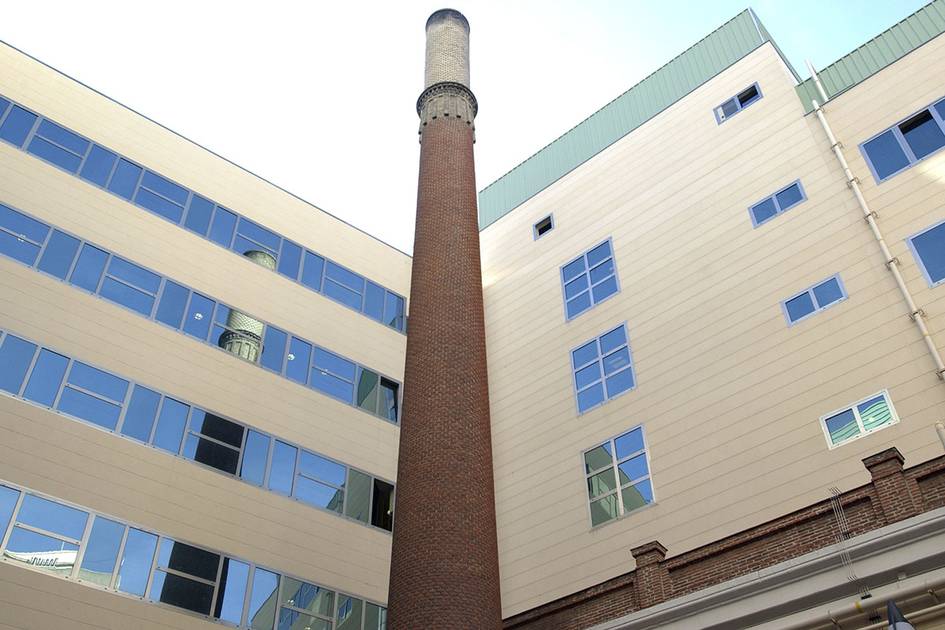 A tall brick chimney stands between modern buildings with multiple windows.