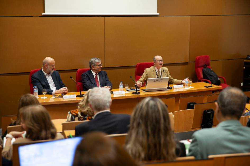 Un panel de discusión con tres ponentes frente a una audiencia en una sala de conferencias.