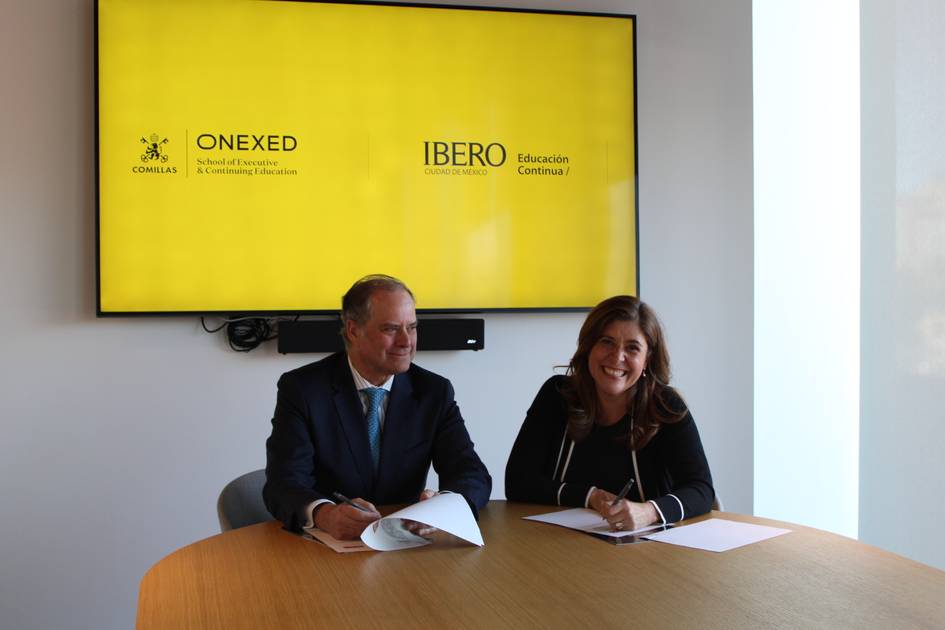 Dos personas sentadas en una mesa firmando documentos con una pantalla de fondo que muestra logotipos de ONEXED e IBERO.