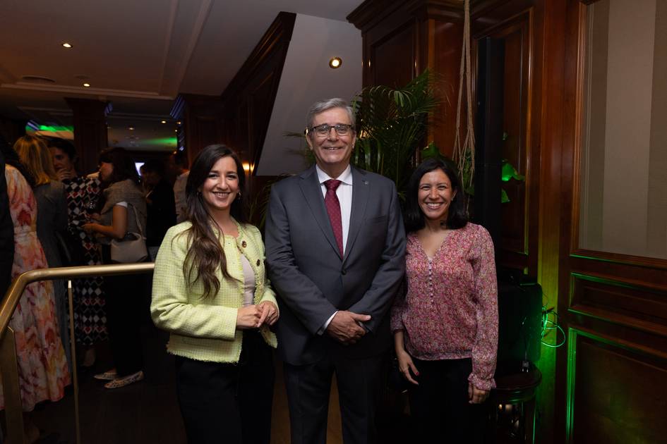 Two women and a man standing together in a formal indoor setting, smiling at the camera.