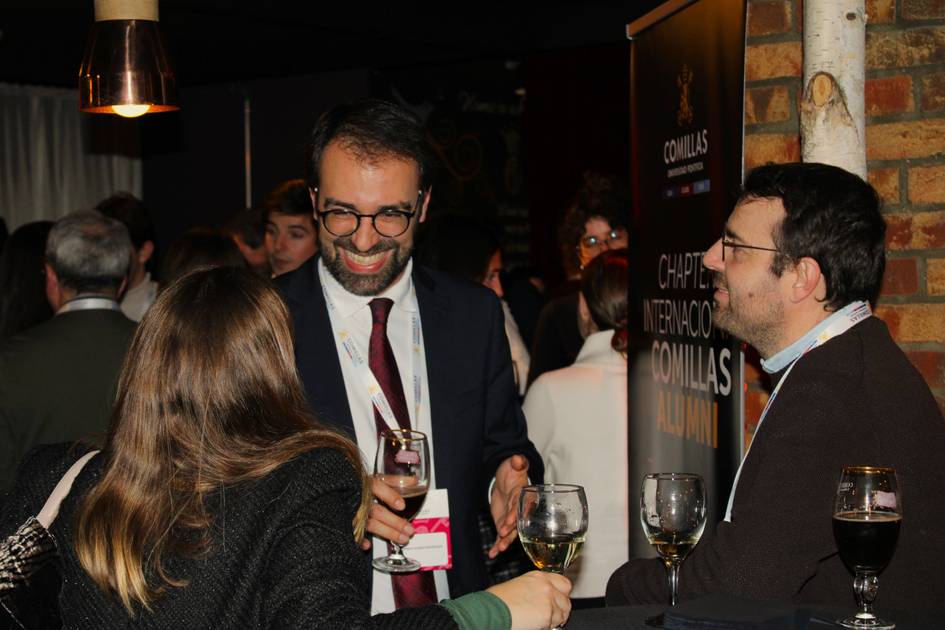 Tres personas conversando alegremente en un evento social con copas de vino en sus manos.