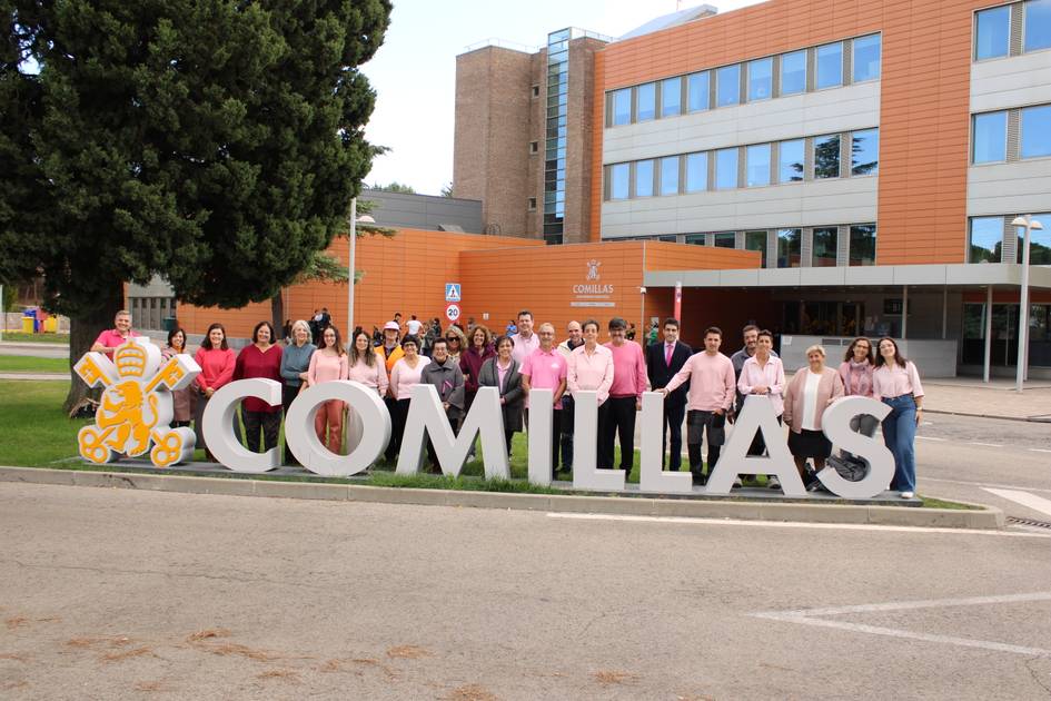 Un grupo de personas vestidas de rosa posando frente al cartel de la Universidad Pontificia Comillas.