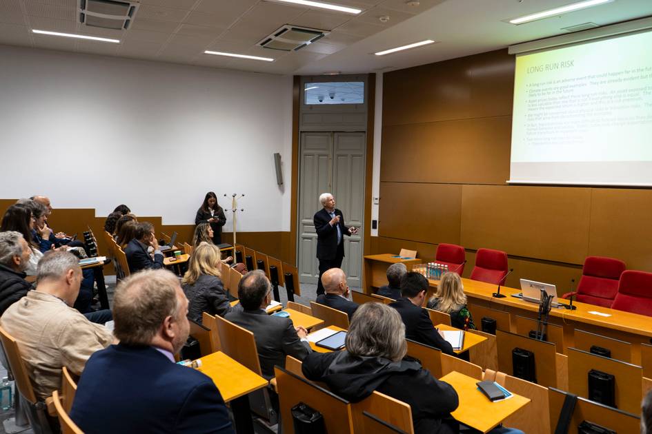 Una sala de conferencias con un ponente frente a un público atento.