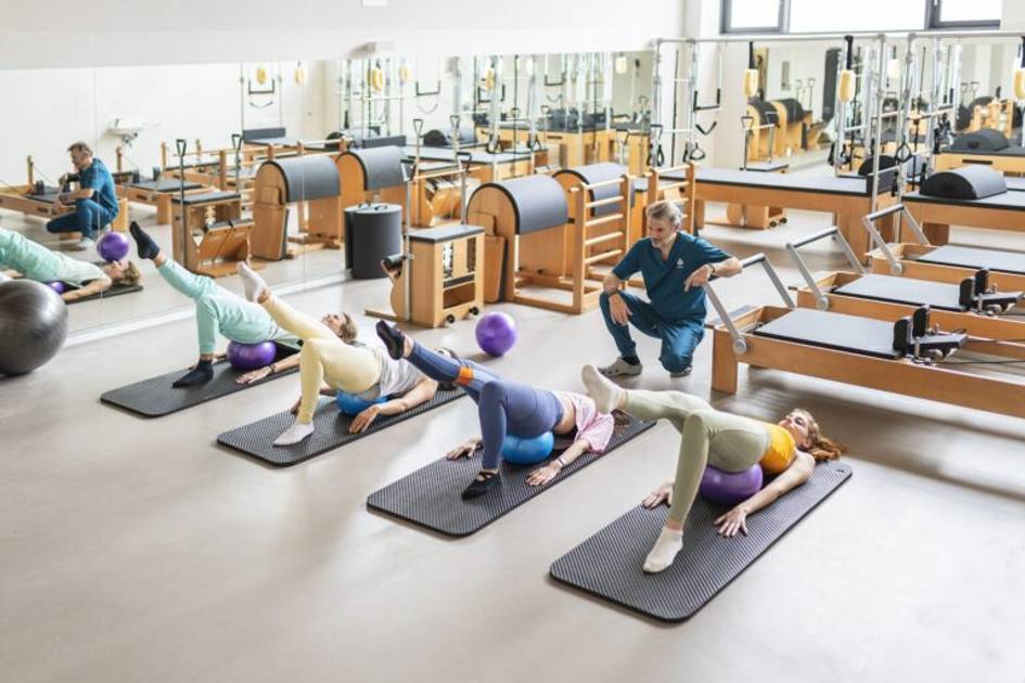A group of people performing exercises on mats at a well-equipped gym, with an instructor guiding them.