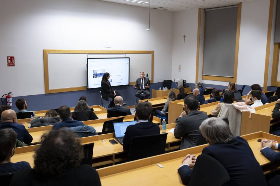 Una conferencia en un aula con un presentador y un panelista ante una audiencia atenta.