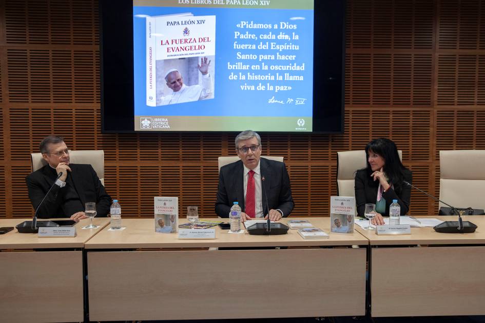 Una mesa de discusión con tres personas hablando sobre un libro del Papa León XIII, con un proyector detrás que muestra una imagen relacionada.