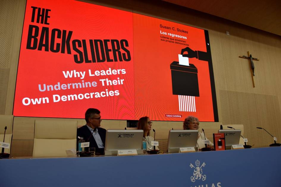 Una presentación en un evento con un panel de discusión y una imagen de fondo que muestra un libro sobre la democracia.