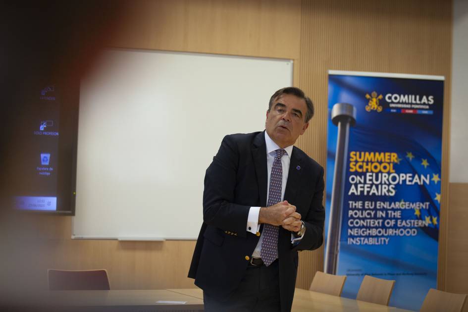 Un hombre vestido con traje habla en una sala de conferencias junto a un cartel de una escuela de verano sobre asuntos europeos.