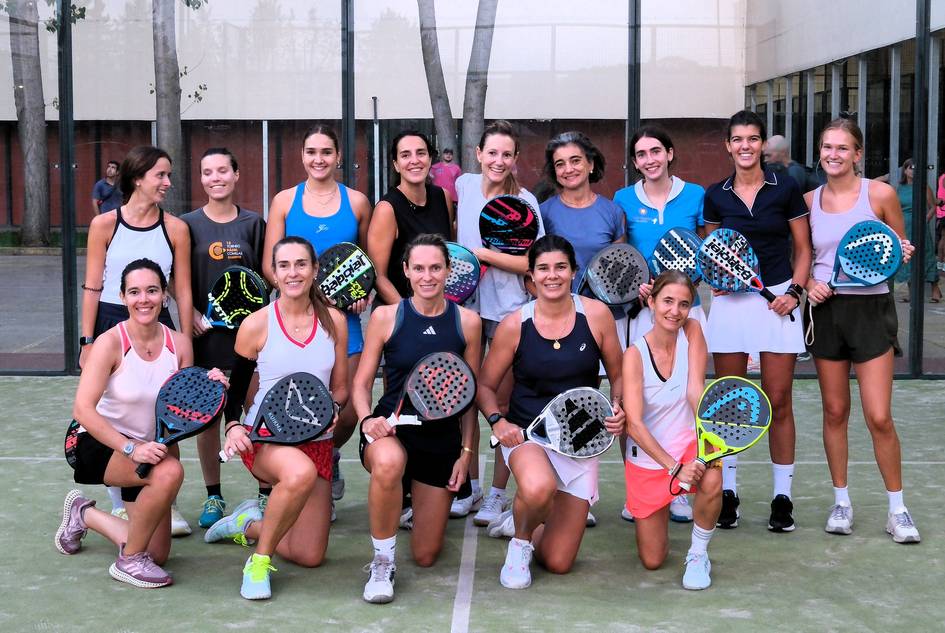 Un grupo de mujeres posando en una cancha de pádel con palas en la mano.