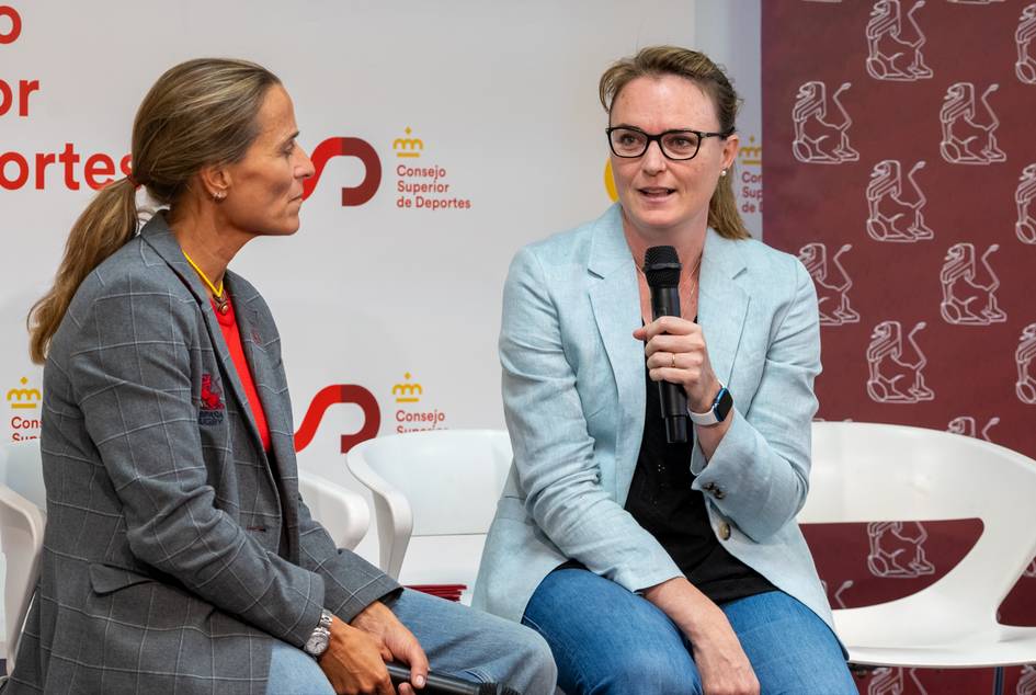 Two women engaging in a discussion at a public event, one speaking and the other listening attentively.