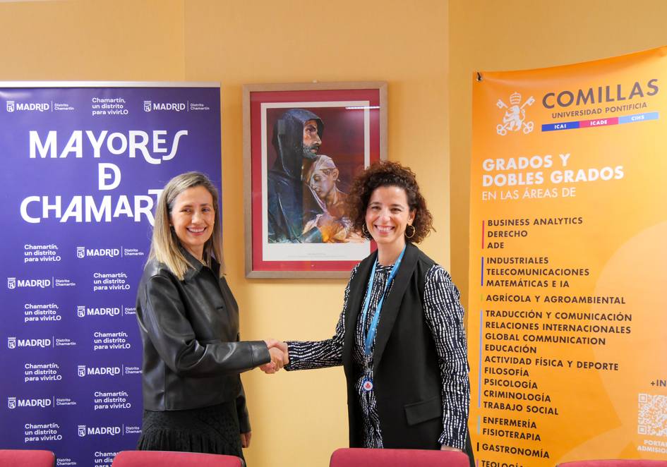 Dos mujeres se dan la mano en un entorno institucional con carteles informativos de programas educativos en la pared.
