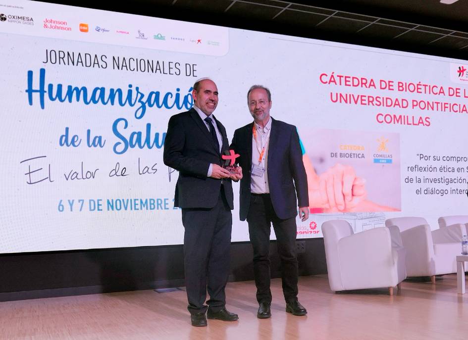 Two men shaking hands on stage at a health conference, with banners about humanization of health in the background.