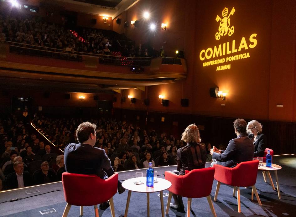 Un evento desarrollado en un auditorio lleno, con varios ponentes sentados en un escenario iluminado por la marca de la universidad.