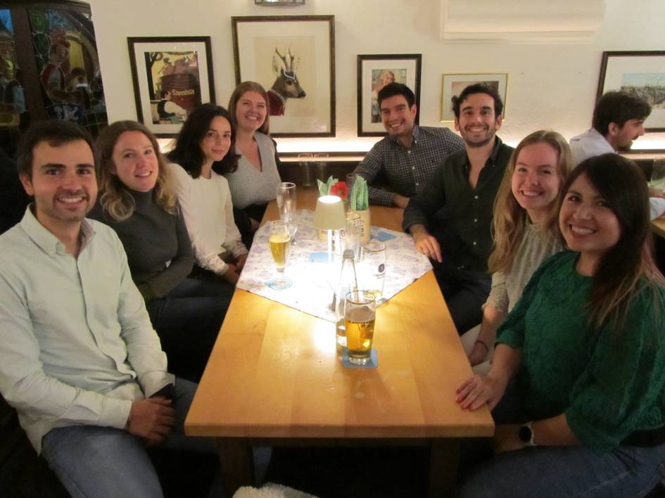 A group of eight people smiling at a table in a restaurant with drinks.