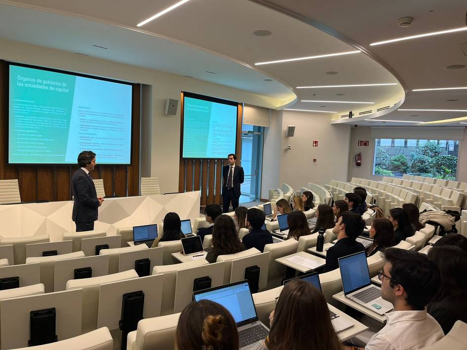 Dos personas están presentando en una sala de conferencias ante una audiencia de estudiantes con computadoras portátiles.