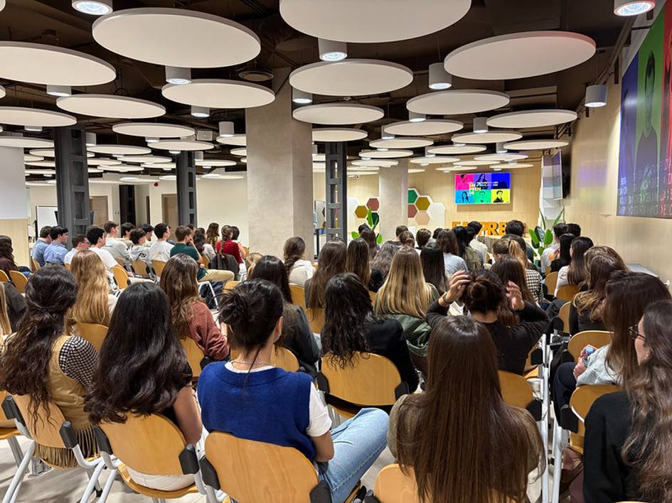 Un grupo de personas sentadas frente a una presentación en una sala moderna.