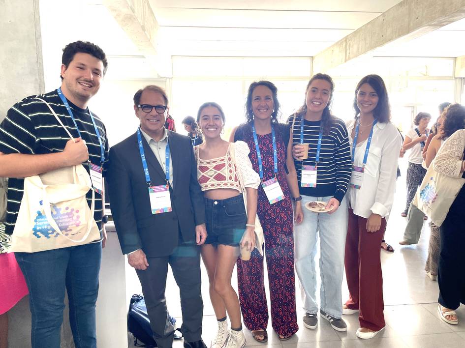 A group of six people, smiling and posing together at a conference, holding event badges.