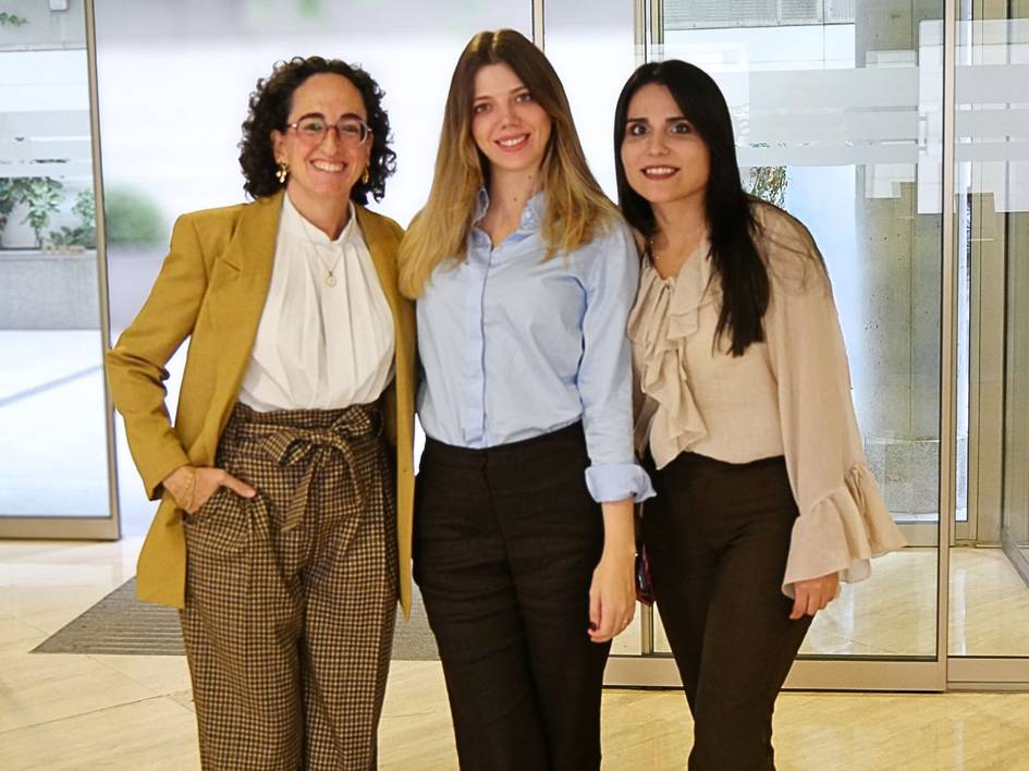 Tres mujeres posan juntas en un ambiente interior luminoso y moderno.