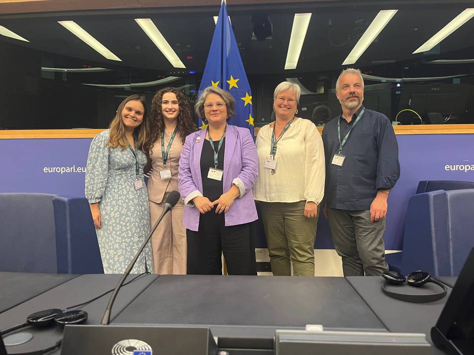 Un grupo de cinco personas posando frente a una bandera de la Unión Europea en un entorno institucional.