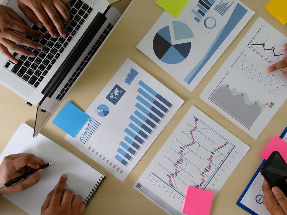 People working at a table with laptops and various business charts spread out