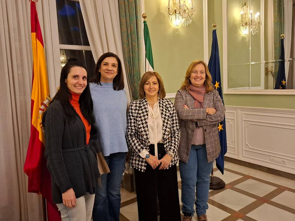 Cuatro mujeres sonriendo, de pie en una sala con banderas de España y la Unión Europea.