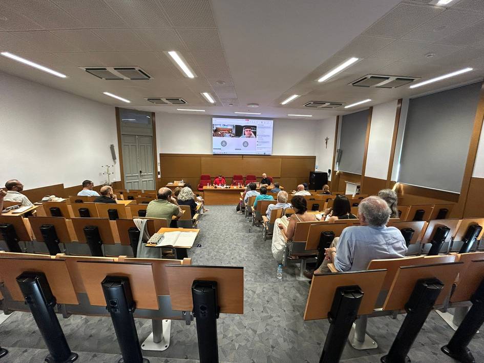 Una sala de conferencias con un grupo de personas sentadas y un panel al frente.