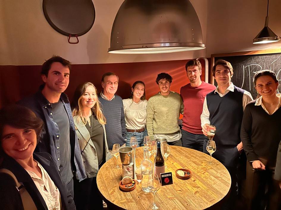 A group of people smiling around a bar table with drinks and snacks in a warmly lit room.