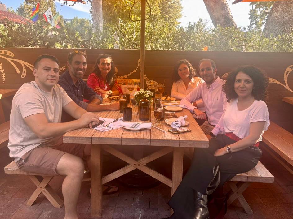 Un grupo de seis personas disfruta de una comida al aire libre en una mesa acogedora.
