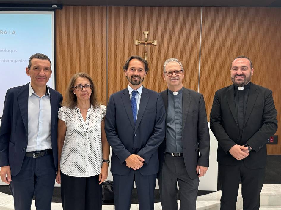 Un grupo de cinco personas posando en un entorno formal con una cruz en la pared de fondo.