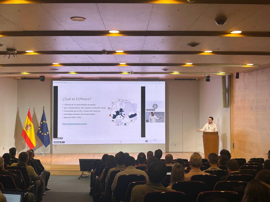 Una presentación en un auditorio con una persona hablando sobre el tema '¿Qué es el EU-Peace?' mientras el público escucha atentamente.