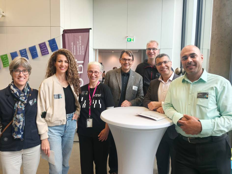 Un grupo de siete personas posando juntas en un evento con mesas y decoración de fondo.