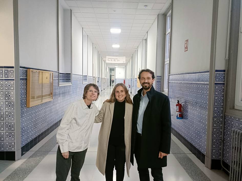 Tres personas sonriendo en un pasillo con paredes decoradas con azulejos azules.