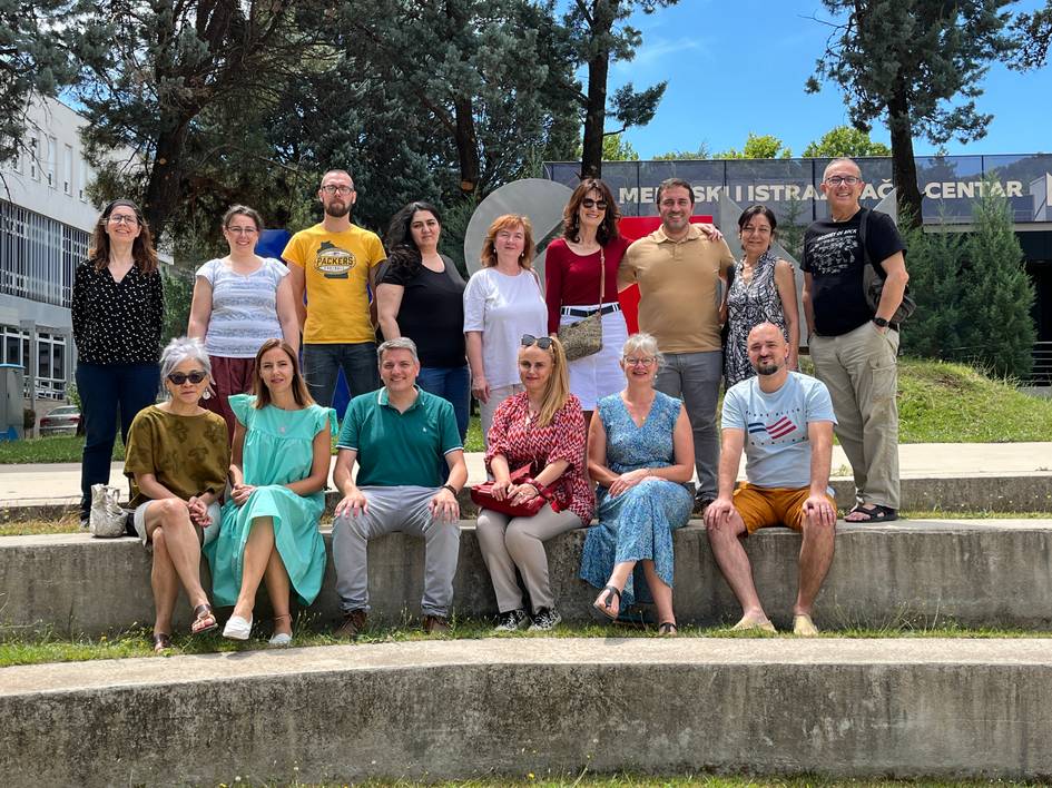 A group of fifteen people posing together in front of a building on a sunny day.