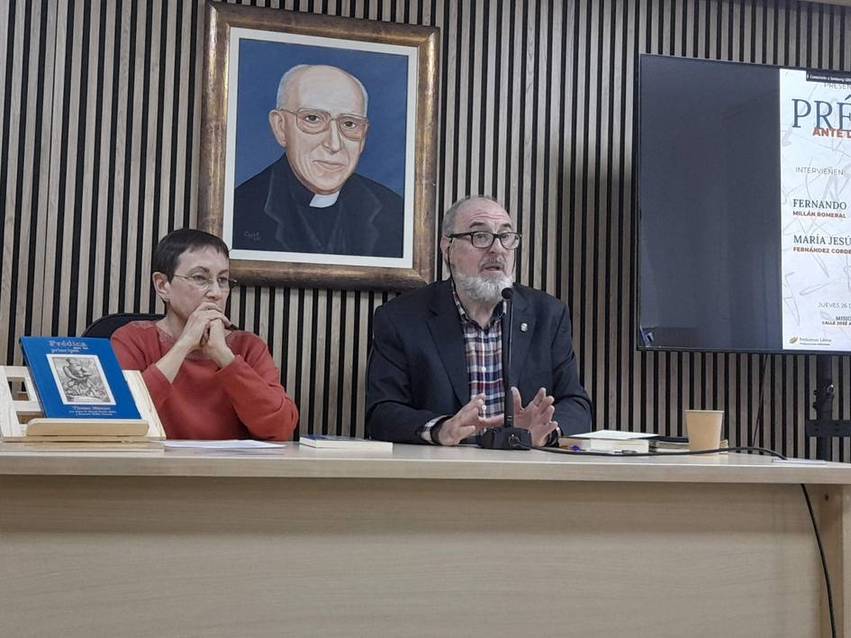 Una presentación en una mesa con un hombre y una mujer, con un retrato en la pared de fondo.