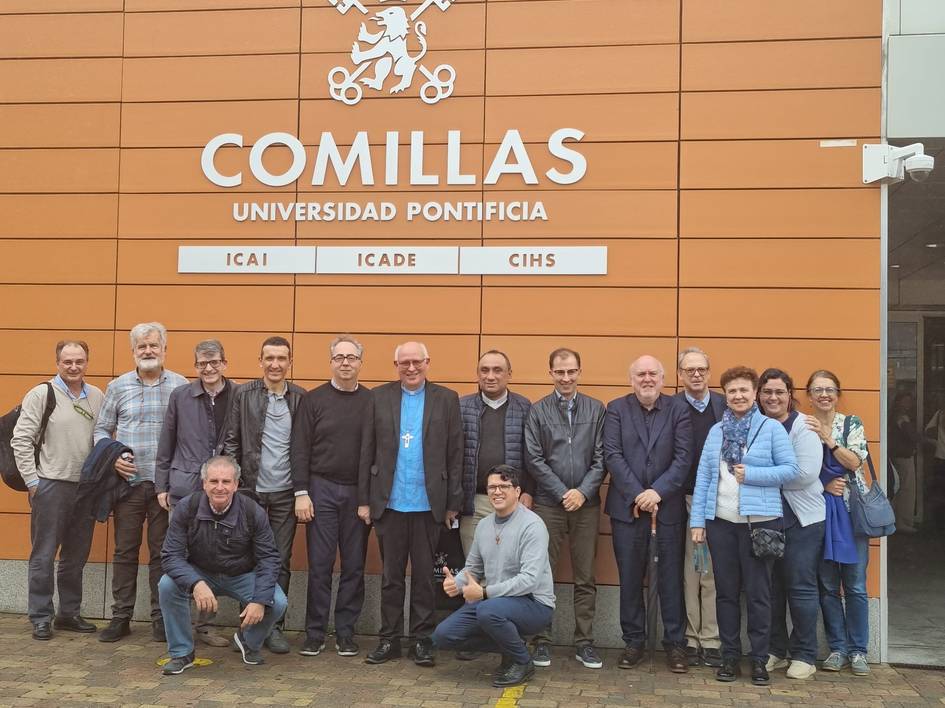 A group of people posing in front of the Comillas Pontifical University sign.