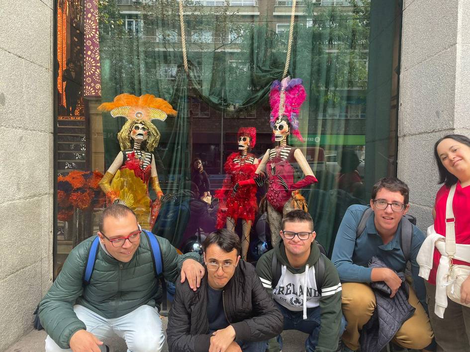 Grupo de personas posando frente a una vitrina decorada con figuras de calaveras para el Día de Muertos.