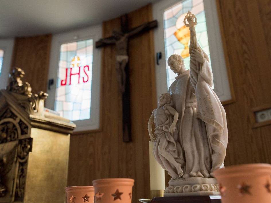 La imagen muestra una estatua religiosa en un altar con vitrales de fondo.