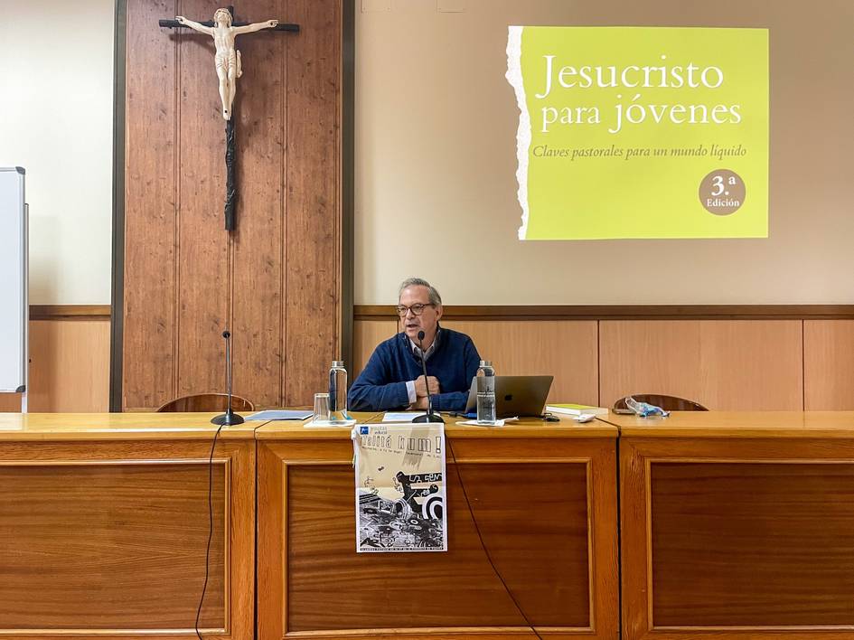 A man is giving a presentation in a room with religious symbols and a poster titled 'Jesucristo para jovenes'.