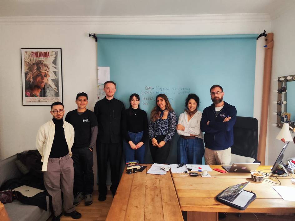 Un grupo de personas posando frente a una pared azul en un entorno de oficina.