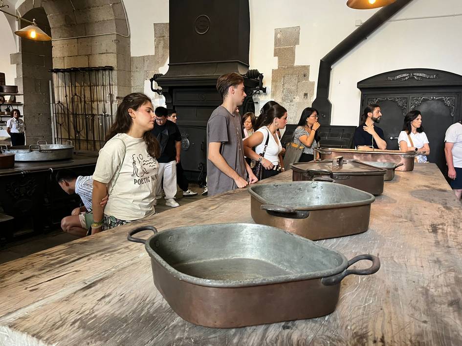 Un grupo de personas observa ollas de metal en una cocina antigua.