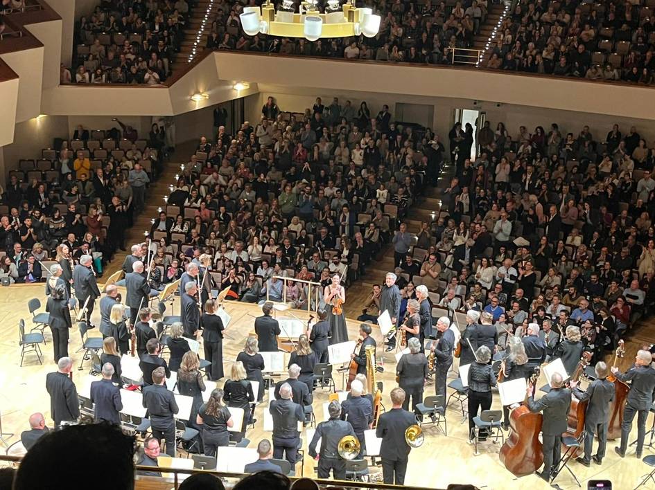 Una orquesta se presenta en un escenario ante un gran público en un auditorio.