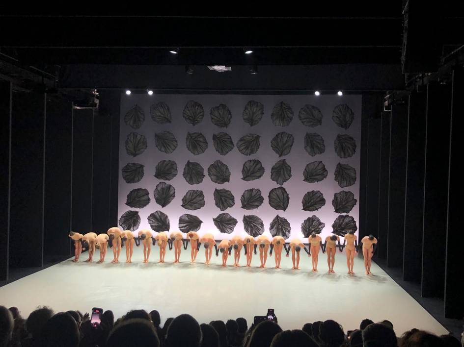 Un grupo de bailarinas se inclina en un escenario con un fondo decorado con hojas.